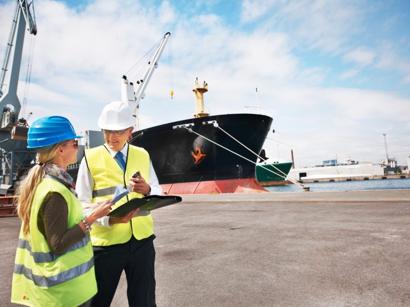 Two dock workers holding paperwork while standing in the shipyard
